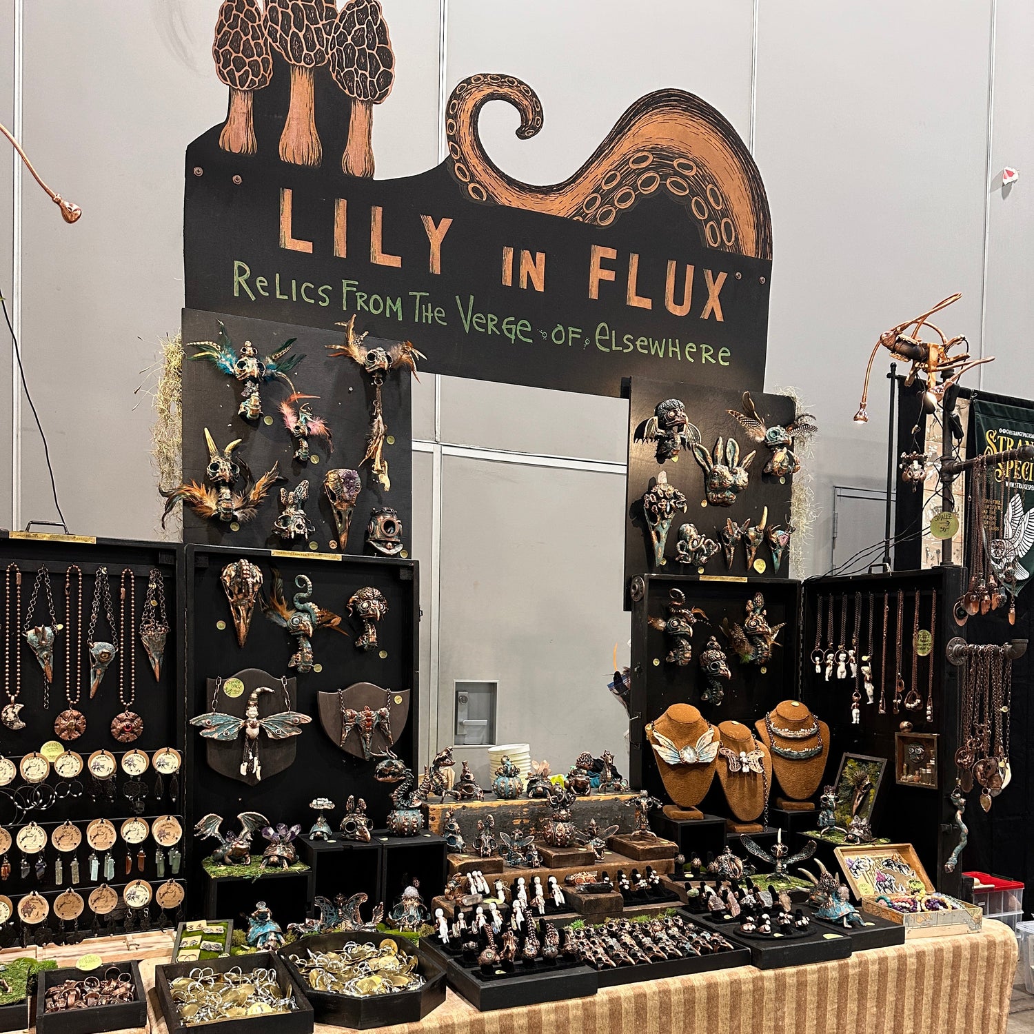 Display of 'Lily in Flux' with various HANDMADE JEWELRY and SCULPTURAL items on a table.